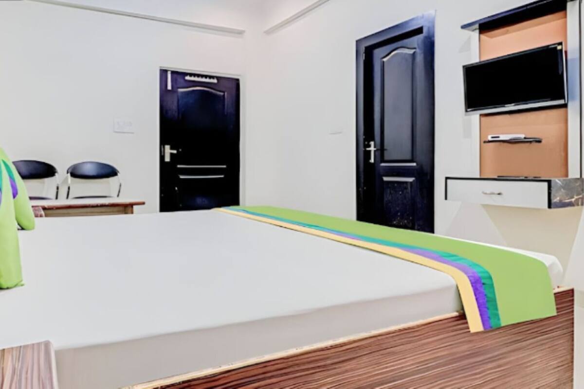 A hotel room with a bed, a desk, a chair, a door, and a television.