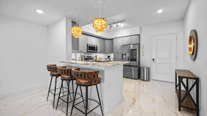 A modern kitchen with a central island, bar stools, stainless steel appliances, and pendant lighting. - RIVER FLY IN: The Merritt, Launchpad Lookout View (Merritt Island)