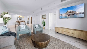 A modern living room with a large TV, two armchairs, a coffee table, and a ceiling fan. - RIVER FLY IN: The Merritt, Launchpad Lookout View (Merritt Island)