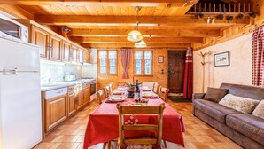 A wooden cabin interior with a dining table set for four, a sofa, wooden cabinets, and a kitchen area. - Chalet 'Chez Mémé' with Mountain View, Private Terrace and Private Garden (Hauteluce)