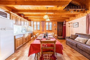 Ein Holzblockhaus-Interieur mit einem für vier Personen gedeckten Esstisch, einer Couch, Holzschränken und einer Küchenzeile.