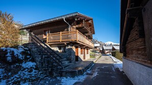 A wooden building with a balcony, stone steps, and a snow-covered ground. - Chalet 'Chez Mémé' with Mountain View, Private Terrace and Private Garden (Hauteluce)