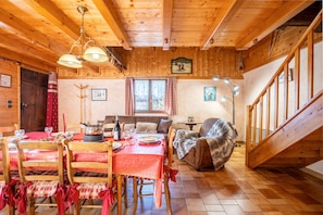Un interior de madera con una mesa de comedor preparada para cuatro personas, un sofá, una silla y una escalera.