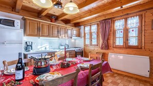 A wooden cabin with a kitchen, dining table set for a meal, and a wine bottle. - Chalet 'Chez Mémé' with Mountain View, Private Terrace and Private Garden (Hauteluce)
