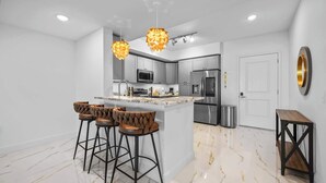 A modern kitchen with a central island, bar stools, stainless steel appliances, and pendant lighting. - RIVER FLY IN: The Merritt, Launchpad Lookout View (Merritt Island)