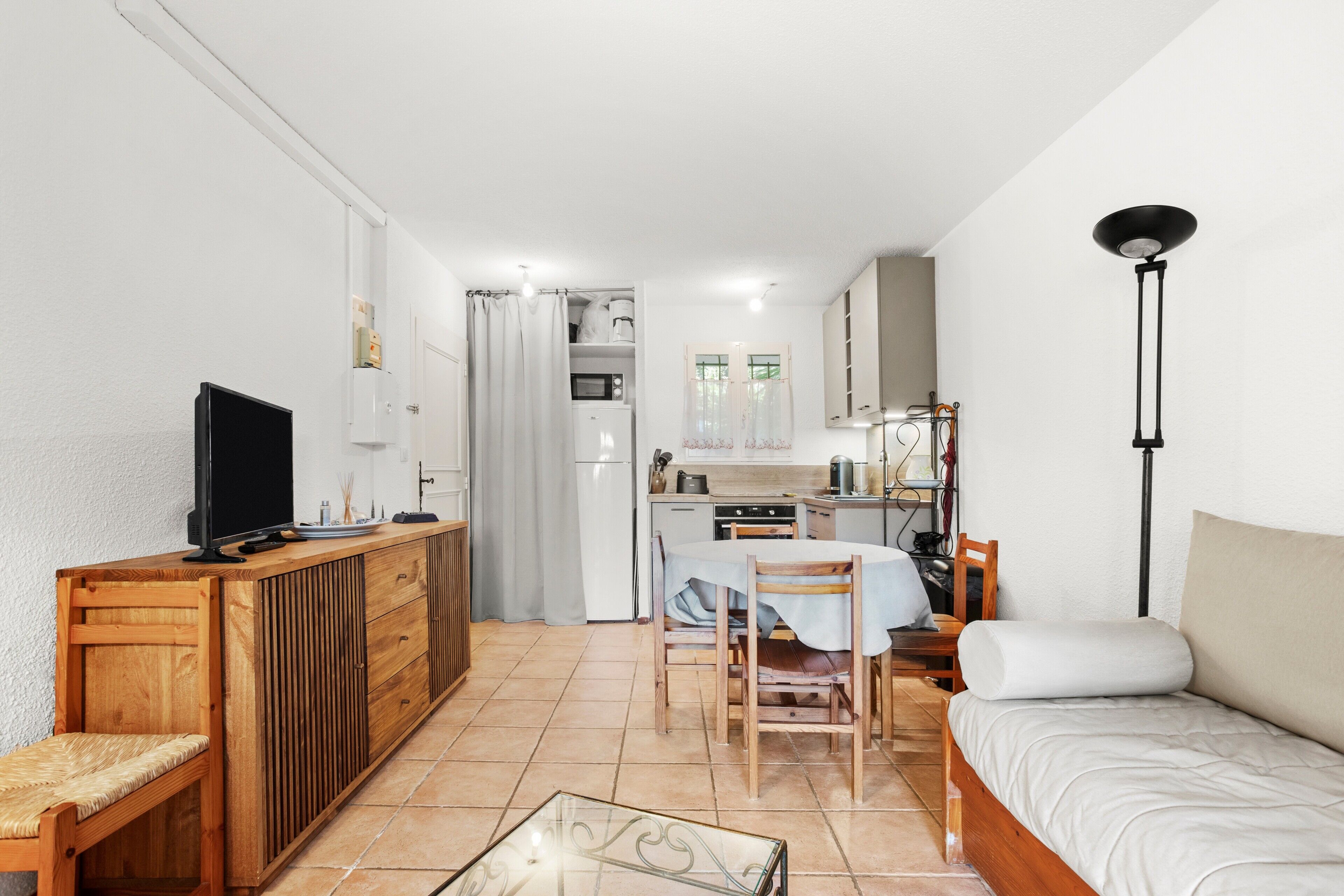 Un espacio habitable compacto con kitchenette, comedor, sofá, televisor y lámpara.