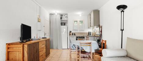 Un espacio habitable compacto con kitchenette, comedor, sofá, televisor y lámpara.