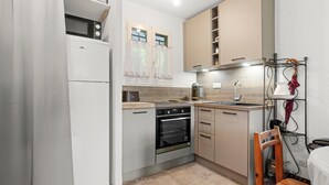 Een kleine keuken met een koelkast, oven, magnetron en een houten stoel.
