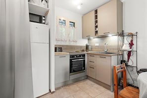 Eine kleine Küche mit Kühlschrank, Backofen, Mikrowelle und einem Holzbstuhl.