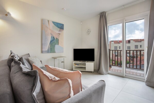 Un salon moderne avec un canapé, un téléviseur à écran plat, un tableau et un balcon offrant une vue sur les immeubles.