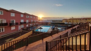 A residential building with a swimming pool, balconies, and a clear view of the sunset.