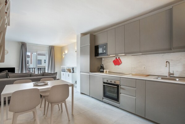 Une cuisine moderne avec des meubles gris, un four à micro-ondes, un four traditionnel et un coin repas comprenant une table et des chaises.