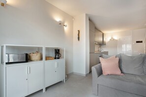 A modern kitchen with white cabinets, a grey sofa with a pink pillow, and a basket on the counter. - Vacation Home 'Ribes' with Sea View, Shared Pool and Wi-Fi (Nuevo Horizonte)