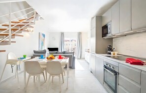 A modern kitchen with stainless steel appliances, a dining area with a high table and chairs, and a staircase with a unique design.
