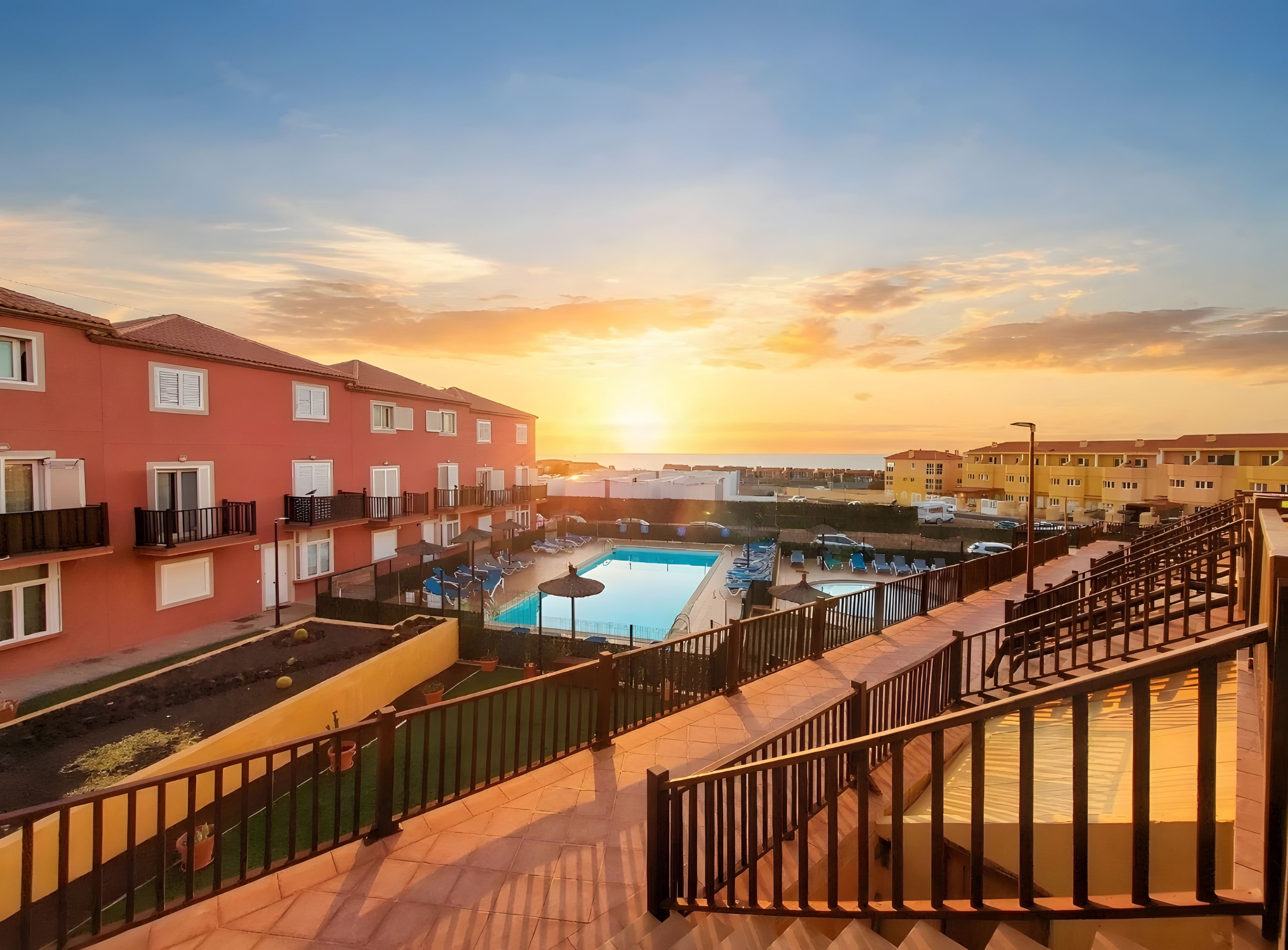 A hotel with a swimming pool, balconies, and a sunset view.
