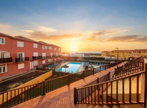 A hotel with a swimming pool, balconies, and a sunset view.