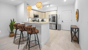 A modern kitchen with a central island, bar stools, stainless steel appliances, and pendant lighting. - RIVER FLY IN: The Meritt, River & Runway View (Merritt Island)