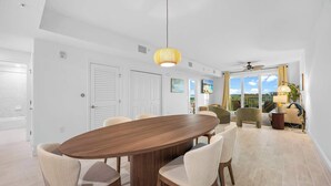 A modern dining area with a wooden oval table, beige upholstered chairs, and a hanging light fixture. - RIVER FLY IN: The Meritt, River & Runway View (Merritt Island)