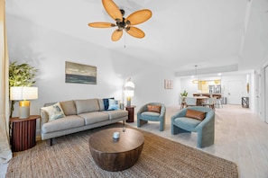 Un salon spacieux comprenant un canapé, des fauteuils, une table basse et un ventilateur de plafond.