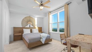 Un dormitorio con cama, escritorio, silla, ventilador de techo y un ventanal con vistas.