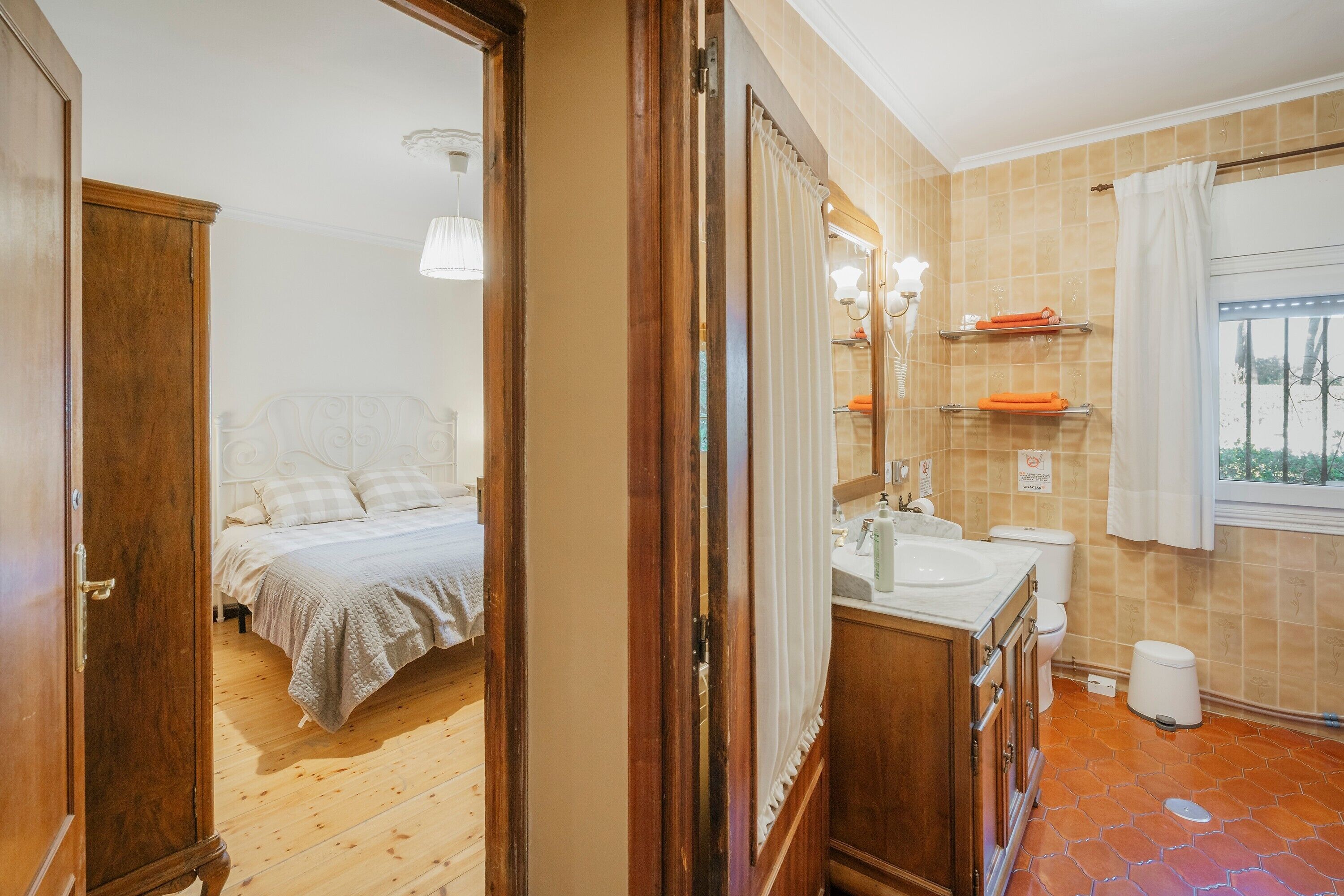A bedroom with a bed, a wooden wardrobe, a bathroom with a sink, toilet, and a window.