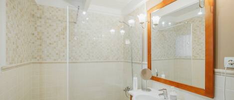 A bathroom with a shower, a sink, a mirror, and a towel rack.