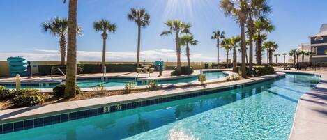 A swimming pool with clear blue water, surrounded by palm trees and a building in the background.