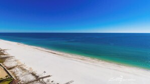 A beach with a clear blue sky and calm sea. There are structures along the beach, possibly for beachgoers. - Phoenix West 1506 (Orange Beach)