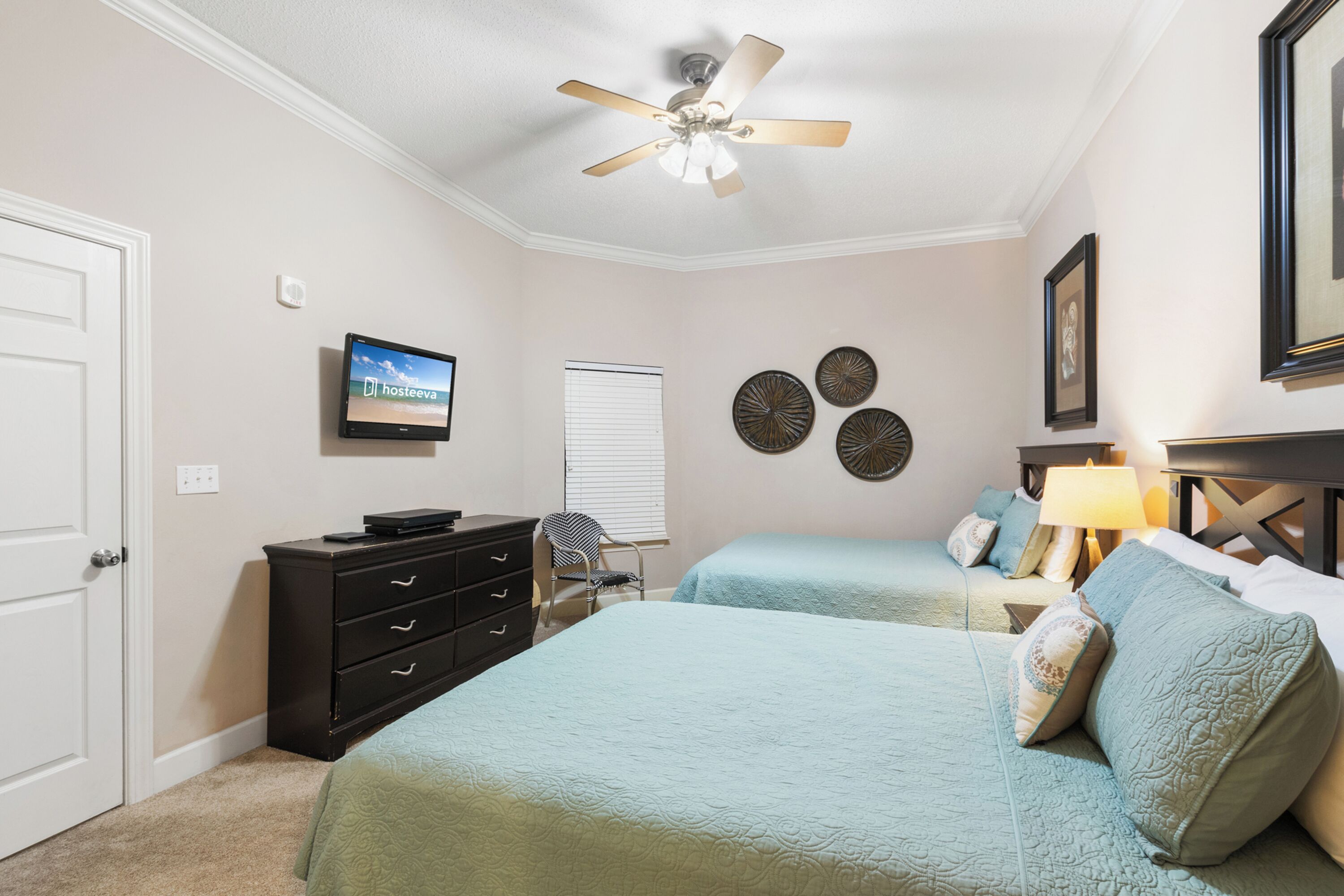 A bedroom with two beds, a ceiling fan, a TV, a dresser, a chair, and decorative wall art.
