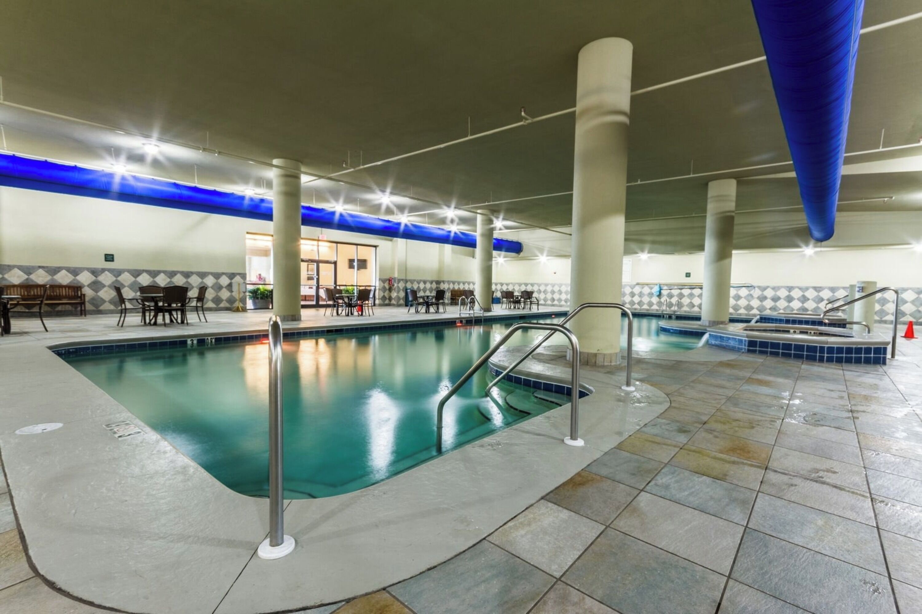 An indoor swimming pool with a tiled floor, metal railings, and a blue ceiling.