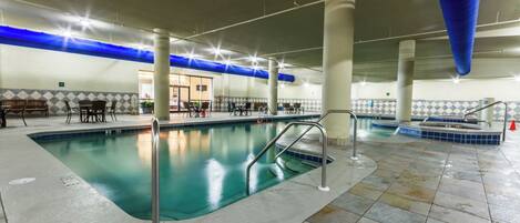 An indoor swimming pool with a tiled floor, metal railings, and a blue ceiling.