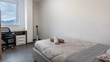 Une chambre à coucher avec un lit, un bureau et une chaise, une fenêtre donnant sur la montagne et un radiateur.