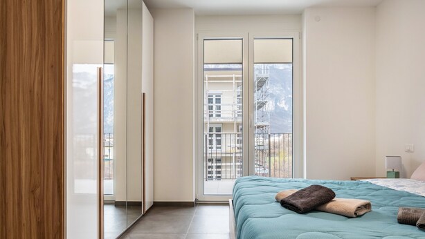 Een slaapkamer met een bed, een raam en uitzicht op gebouwen.