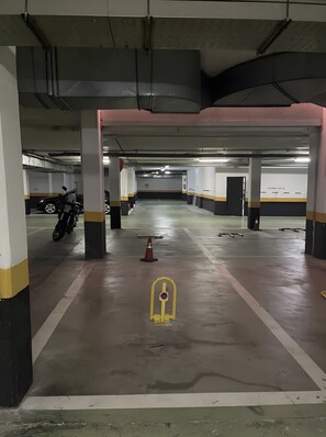 A multi-level parking garage with concrete pillars, a yellow keypad lock on the floor, and a motorcycle parked in the left lane.