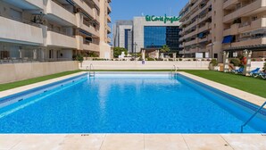 A swimming pool with a clear blue water, surrounded by a well-maintained lawn and a building with balconies.