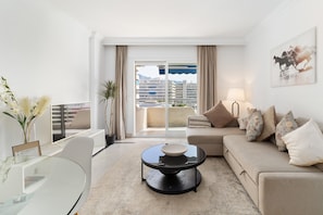 A modern living room with a sofa, coffee table, and a view of buildings through large windows. - Apartment 'Sunresting  Puerto Banus' with Sea View, Wi-Fi and Air Conditioning (Marbella)