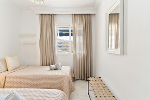 Ein Hotelzimmer mit Bett, einer Sitzbank, einem Fenster mit Vorhängen und Blick auf Gebäude.