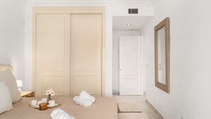 A hotel room with a bed, towels, a tray with cups and a book, a mirror, and a door leading to another room.