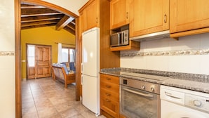 Una cocina con armarios de madera, microondas integrado, refrigerador, horno y lavavajillas.