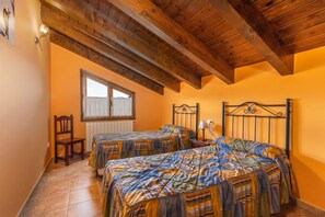 Una habitación con dos camas, vigas de madera en el techo, una ventana con cortinas y un radiador.