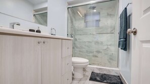 A modern bathroom with a glass shower enclosure, a white toilet, and a wooden vanity.