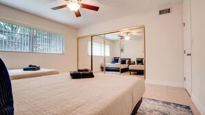 A bedroom with a bed, a ceiling fan, a window with blinds, and a sliding door leading to another room.