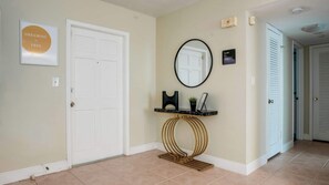 Un couloir avec une porte blanche, un cadre contenant une citation inspirante, un miroir rond, un petit panneau noir et une console avec un plateau en marbre.