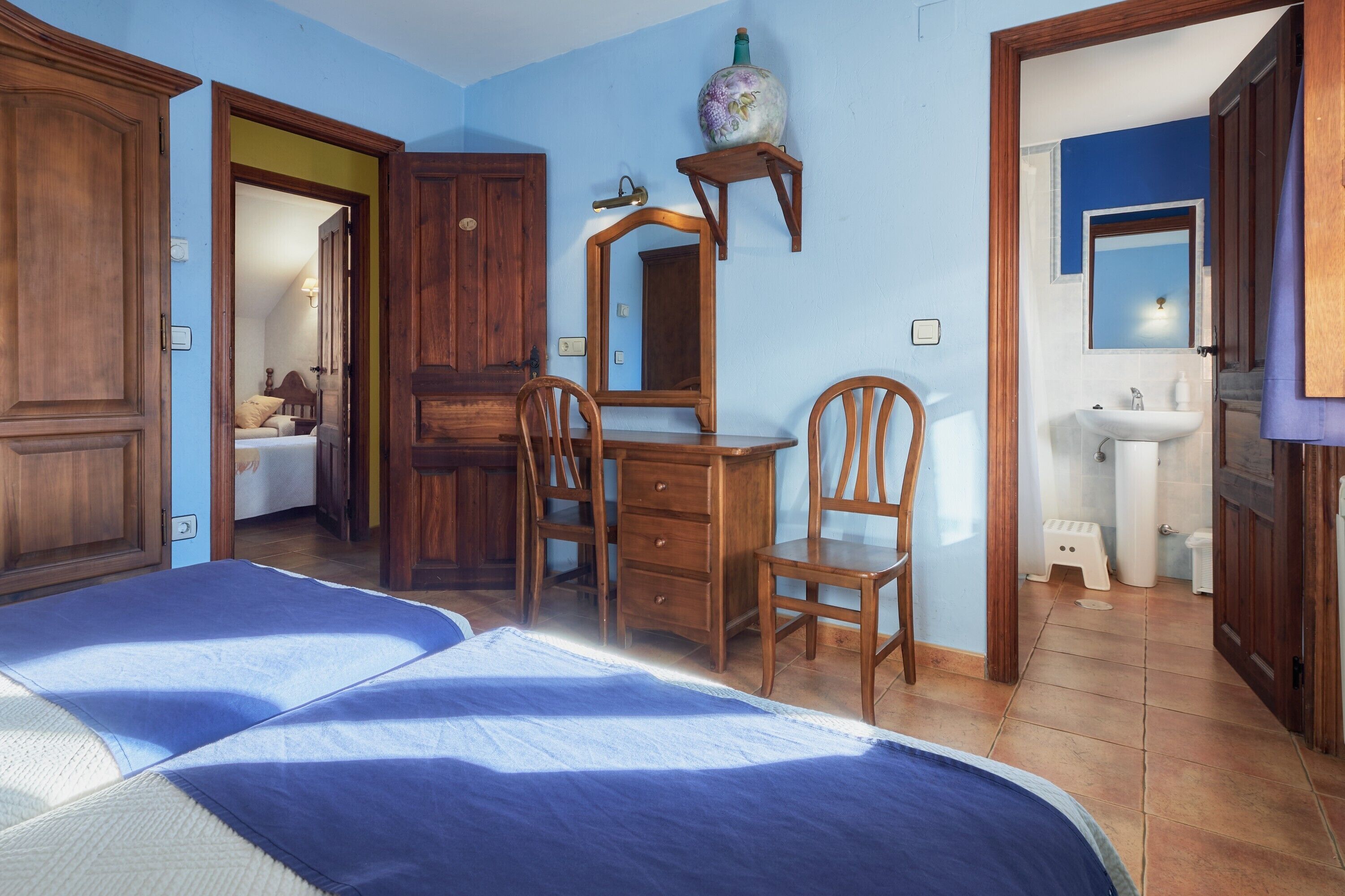 Un dormitorio con dos camas, muebles de madera, un aparador, un espejo y un baño con lavabo e inodoro.