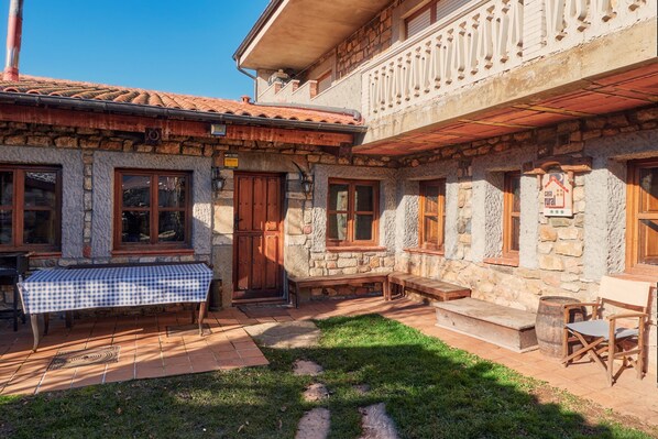 Un edificio de piedra con una mesa a cuadros, bancos de madera y un balcón.