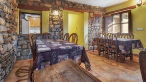 A dining area with a wooden table and chairs, stone walls, and a view of the kitchen. - Country House 'Aldaron' with Mountain View, Private Garden and Wi-Fi (BOCA DE HUERGANO)