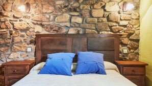 A bed with a wooden headboard, two blue pillows, and a stone wall behind. - Country House 'Aldaron' with Mountain View, Private Garden and Wi-Fi (BOCA DE HUERGANO)