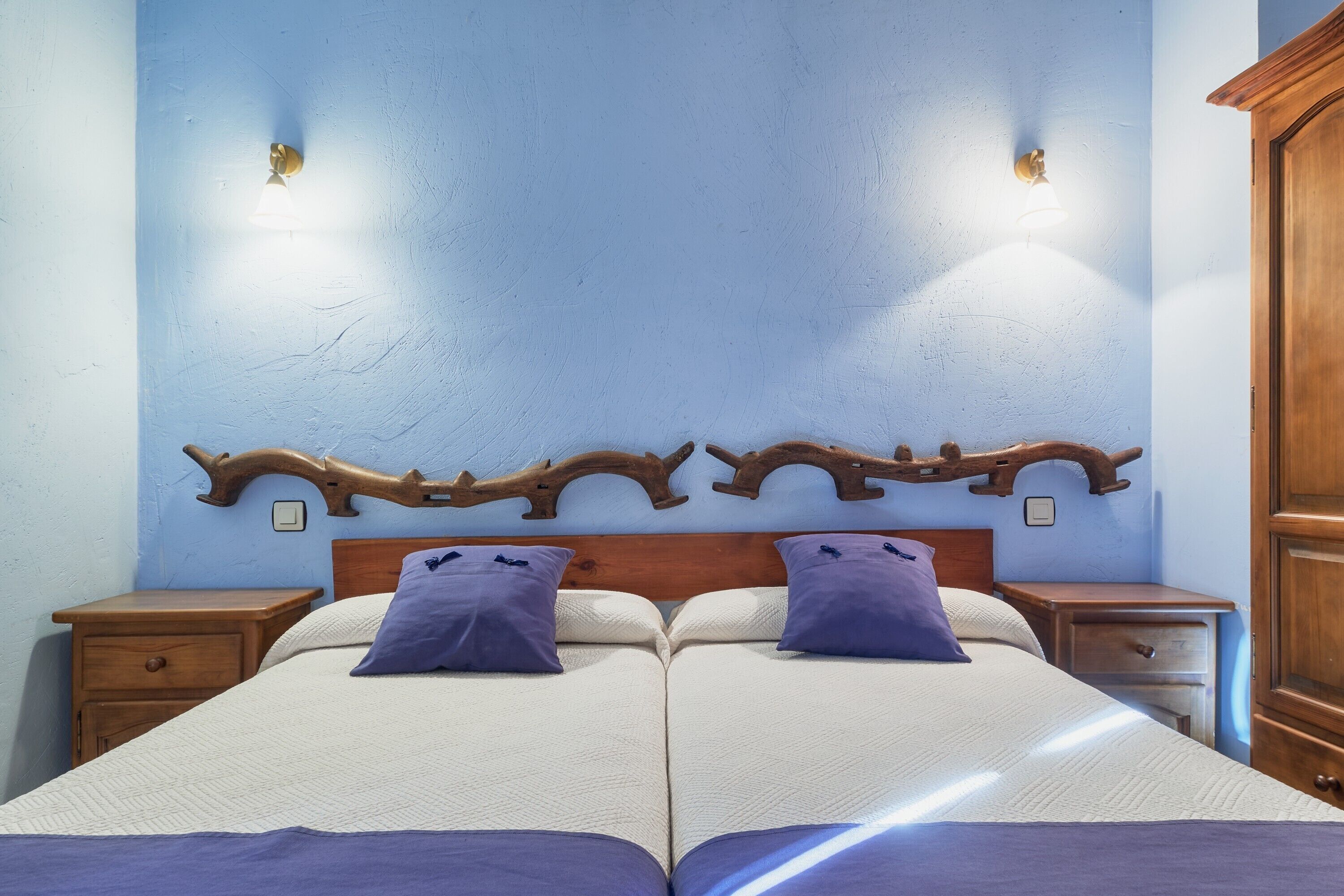 Una cama doble con dos mesitas de noche, cabecera de madera y lámparas fijadas a la pared.