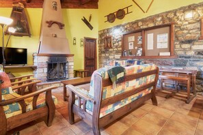 Un interior rústico con pared de piedra, muebles de madera, chimenea y televisor.