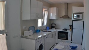 A compact kitchen with a washing machine, microwave, oven, and a dining area with a table set for two. - Country House 'Daniela 2' with Sea View, Wi-Fi and Air Conditioning (El Pozo de los Frailes)